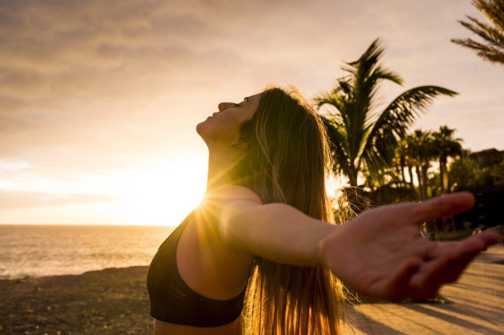 Healthy people lifestyle enjoying sunset and fitness activity alone - beautiful woman feel the sun and the ocean oxygen after workout sport session class - open arms and freedom breathe